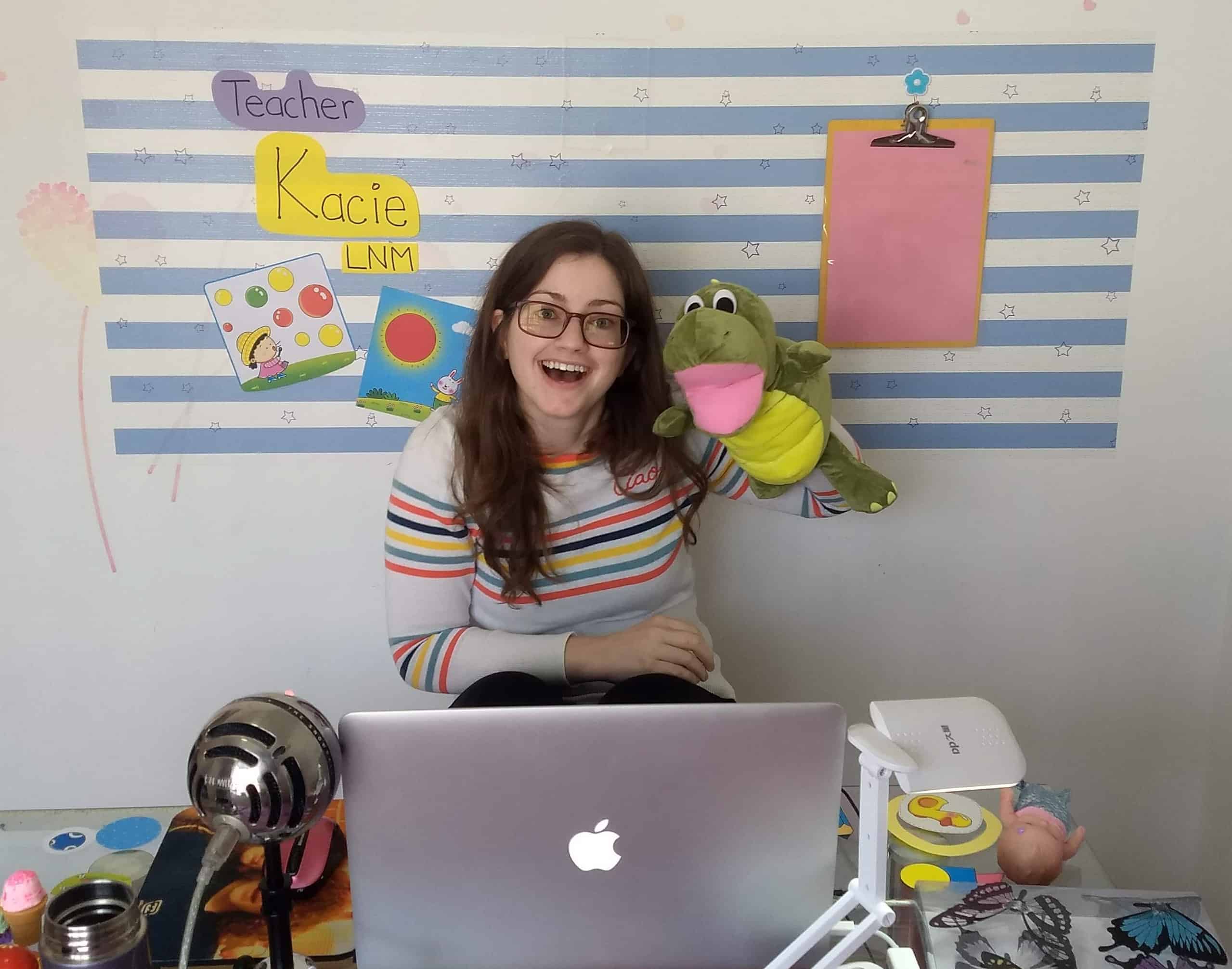 Kacie in her online ESL classroom with a dinosaur puppet